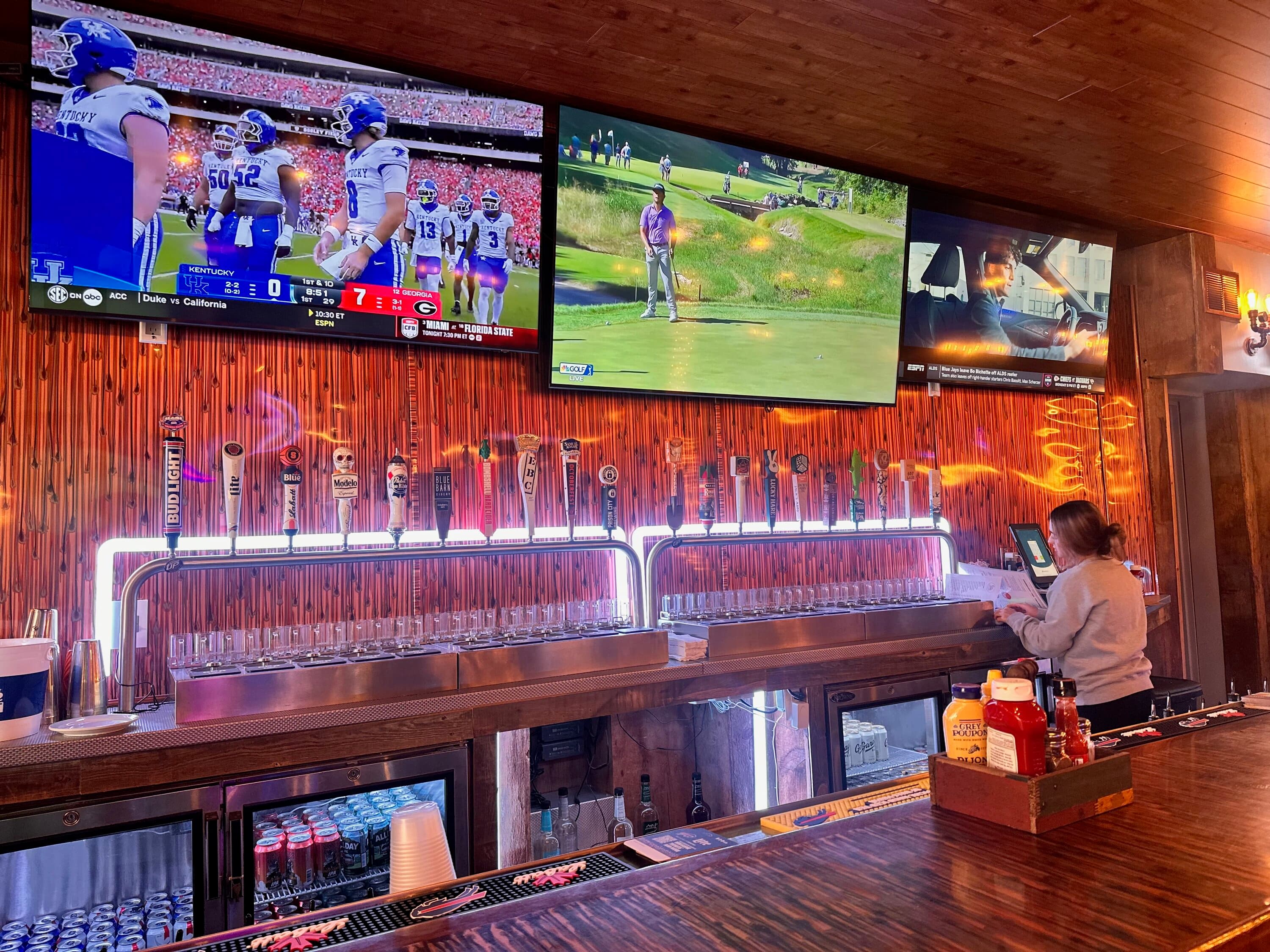 Bar counter with numerous beer taps and multiple TV screens showing sports