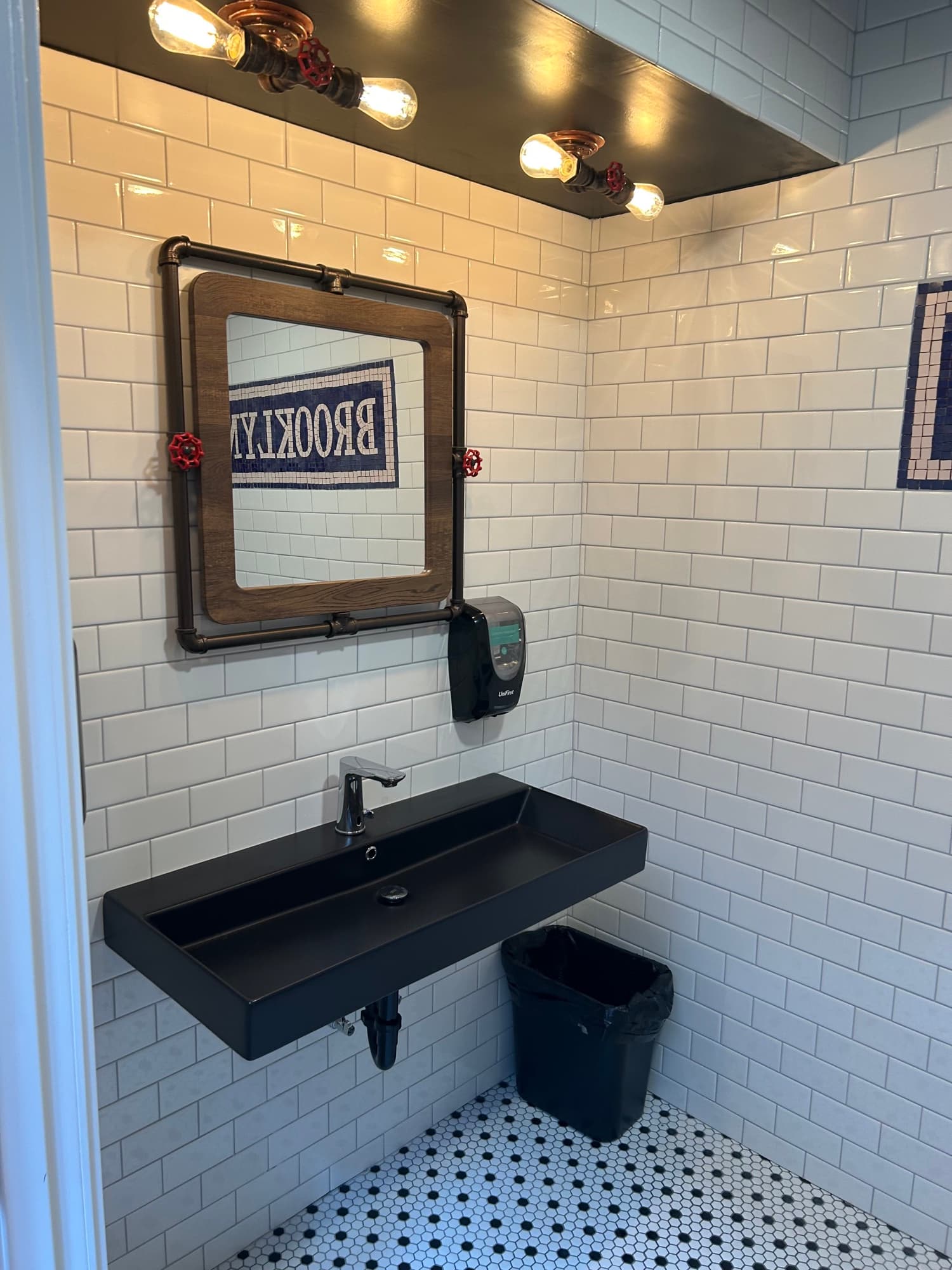 Industrial bathroom with white subway tile, black sink, pipe mirror frame, and mosaic floor