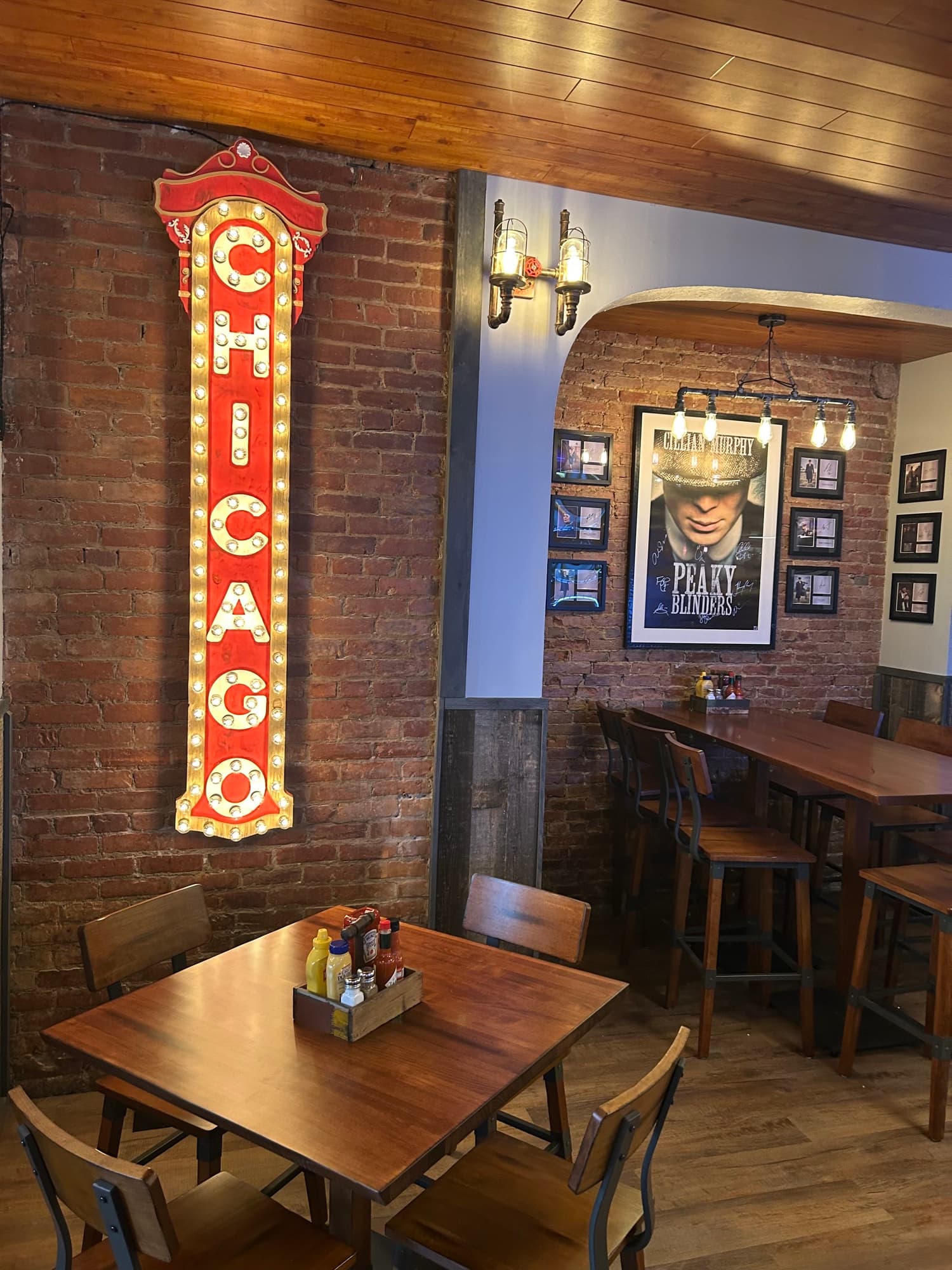 Vintage-style illuminated CHICAGO marquee sign on exposed brick wall with Peaky Blinders poster