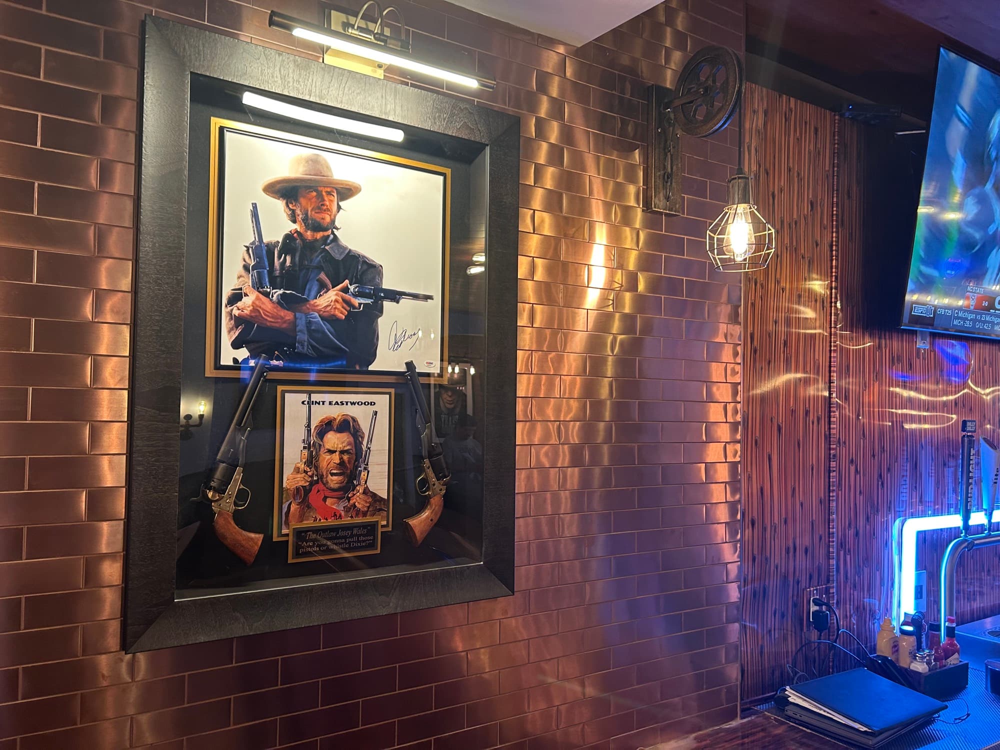 Framed Clint Eastwood western movie posters and rifles mounted on copper tile wall