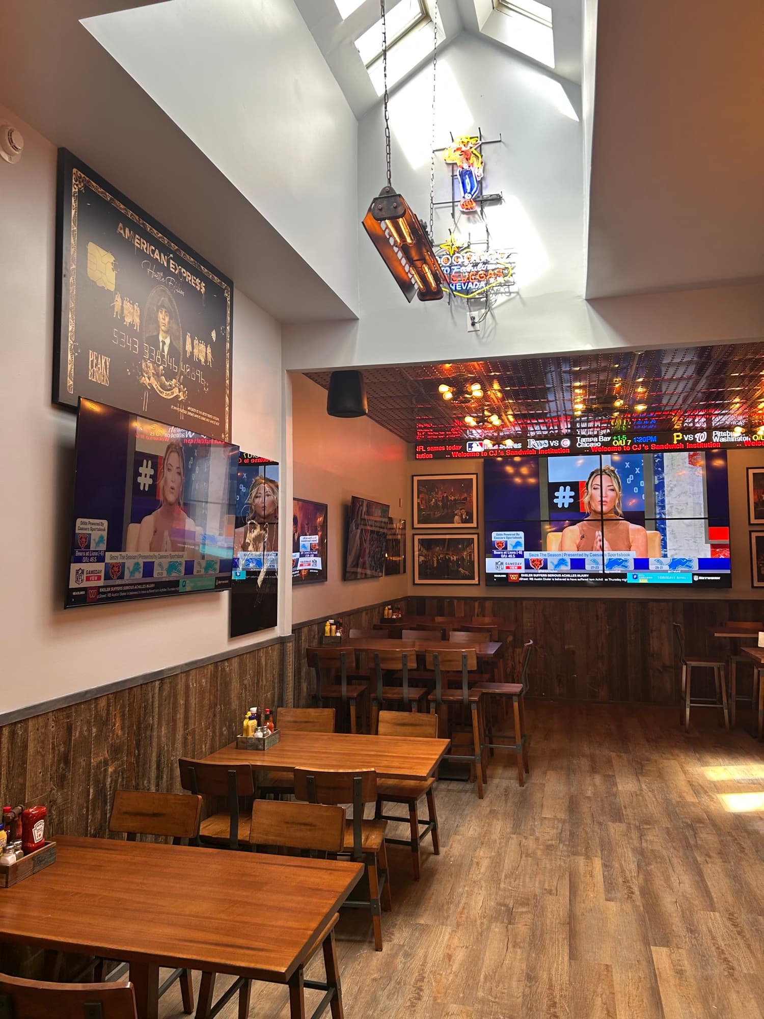 Dining room with wooden tables, skylight, neon signs, and sports screens