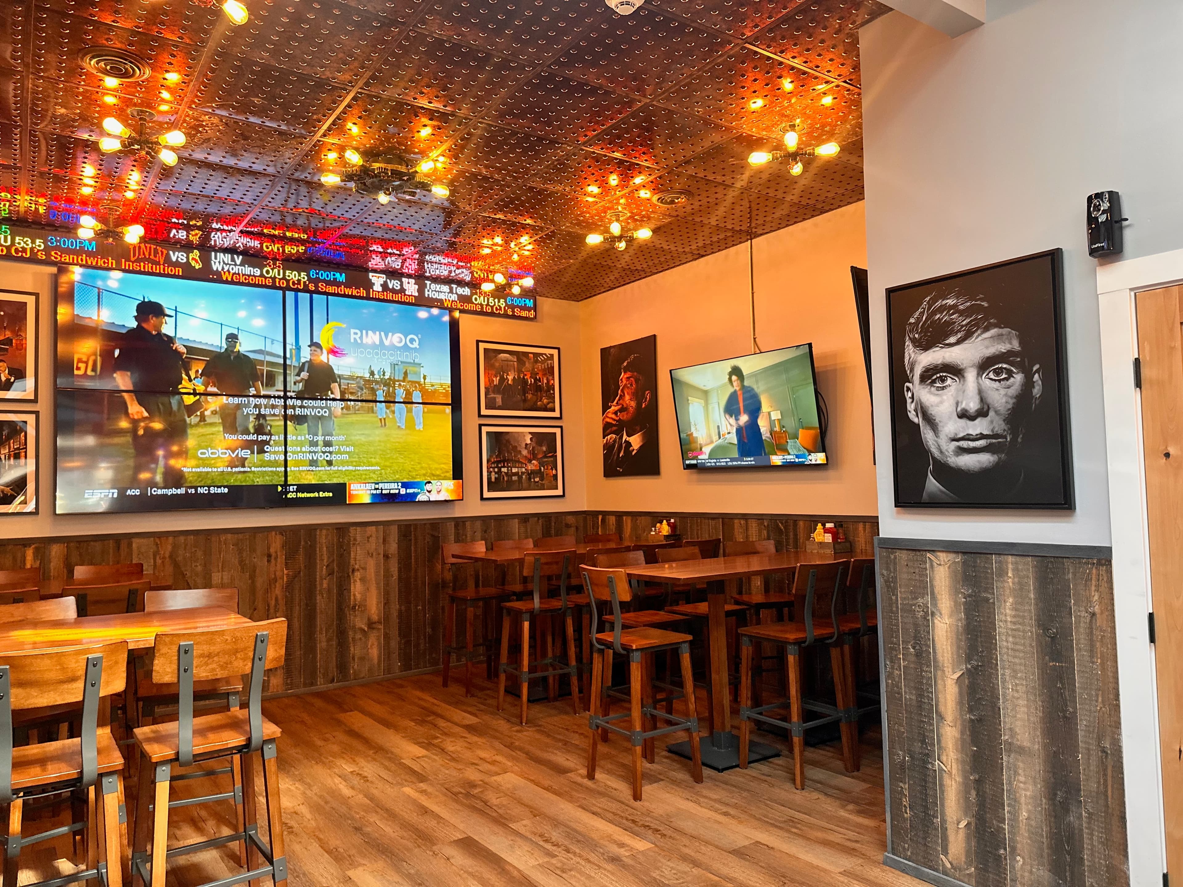 Restaurant dining room with decorative ceiling, sports screens, wooden tables, and framed portraits