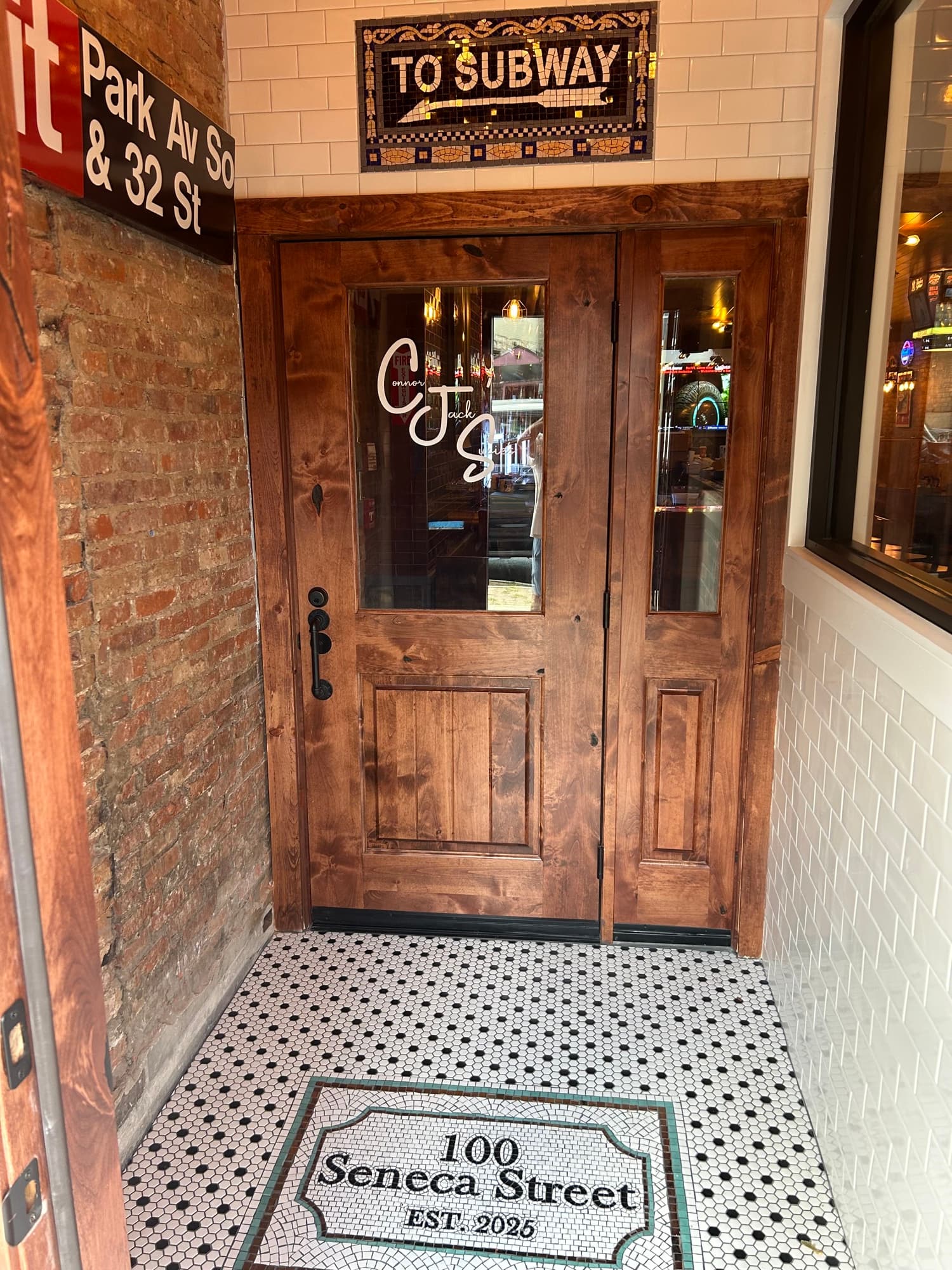 Wooden entrance door with 'TO SUBWAY' mosaic sign and '100 Seneca Street EST. 2028' floor tile