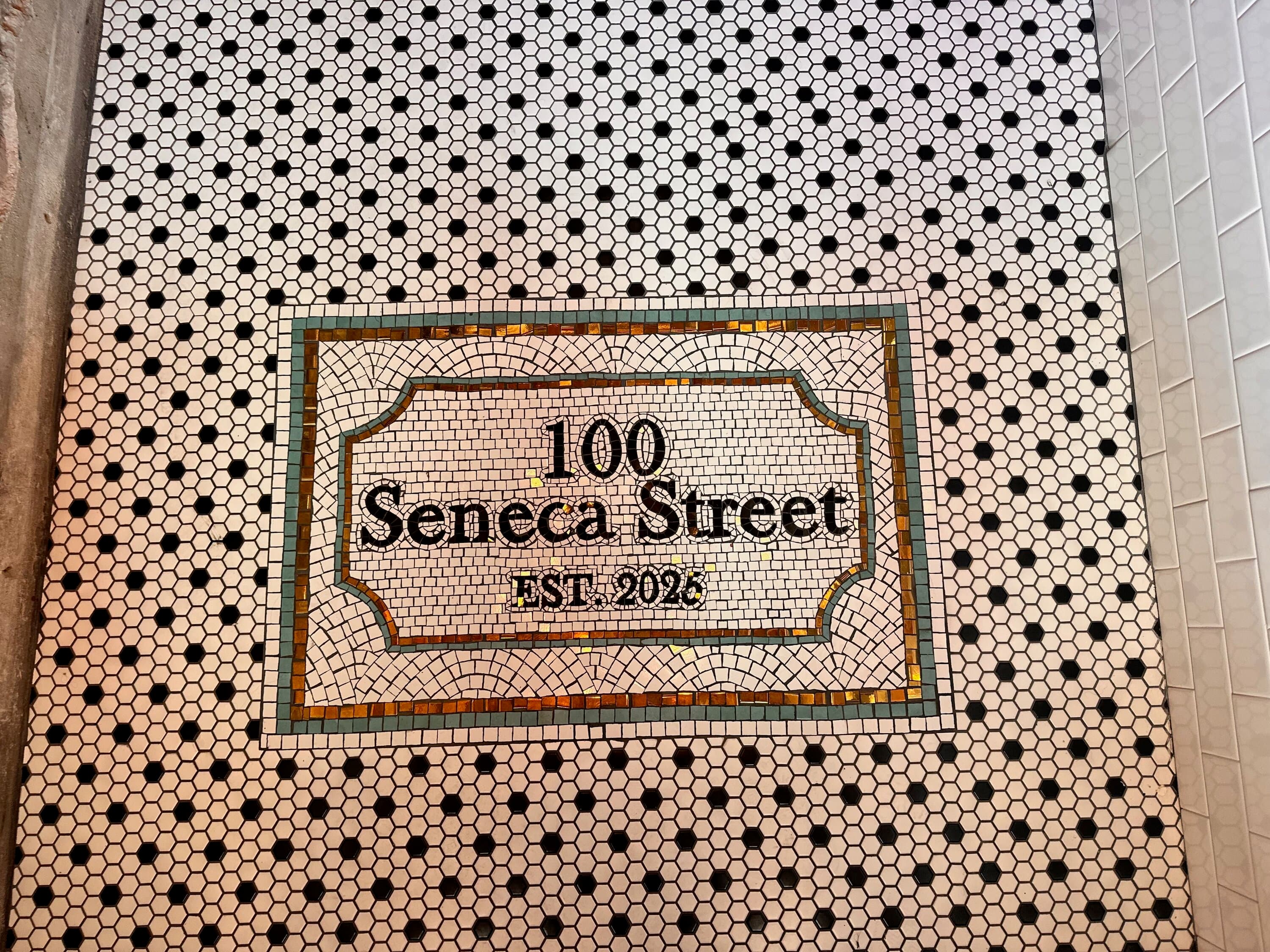 Mosaic tile floor reading '100 Seneca Street EST. 2023' at restaurant entrance