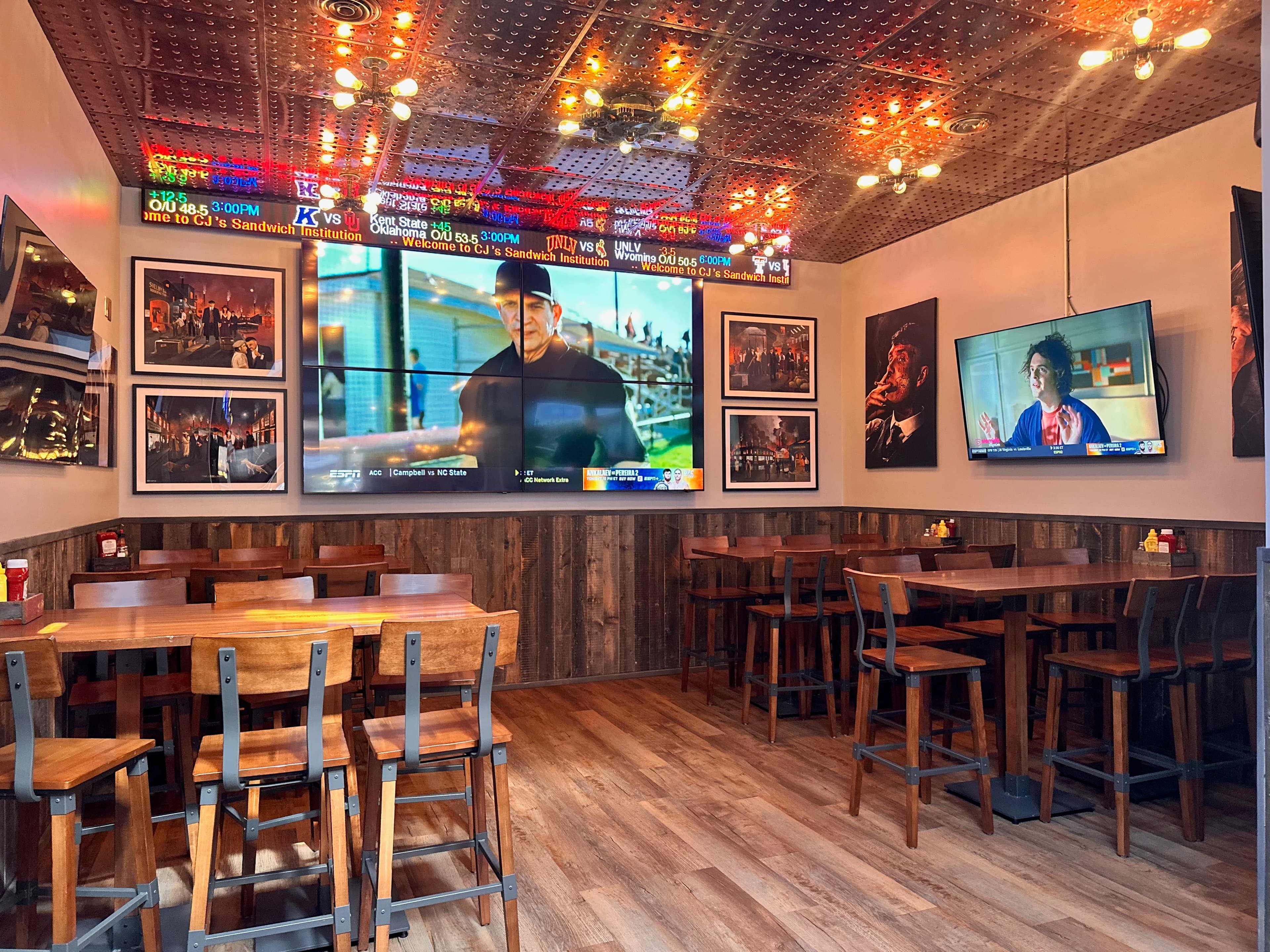 Interior dining area with wooden tables, multiple TV screens showing sports, and decorative ceiling lights