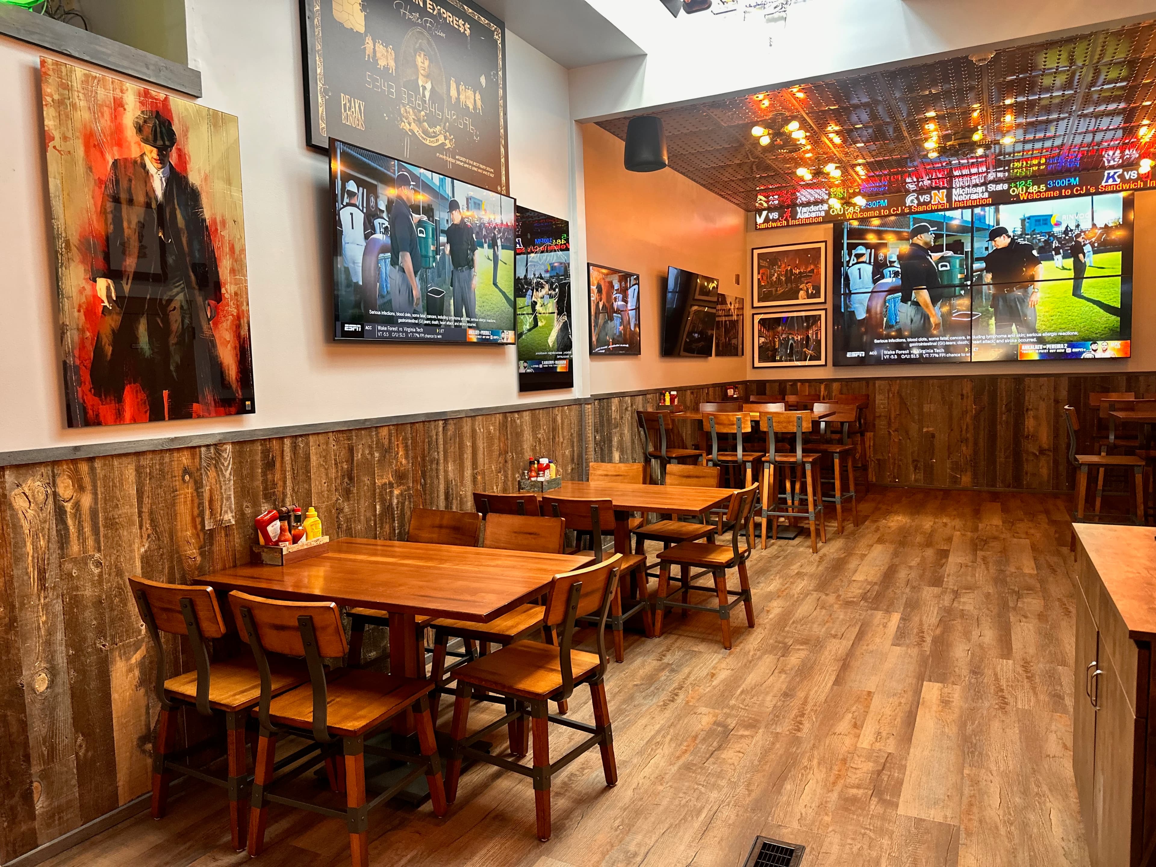 Dining room with wooden tables, rustic wood paneling, and large TV screens showing sports