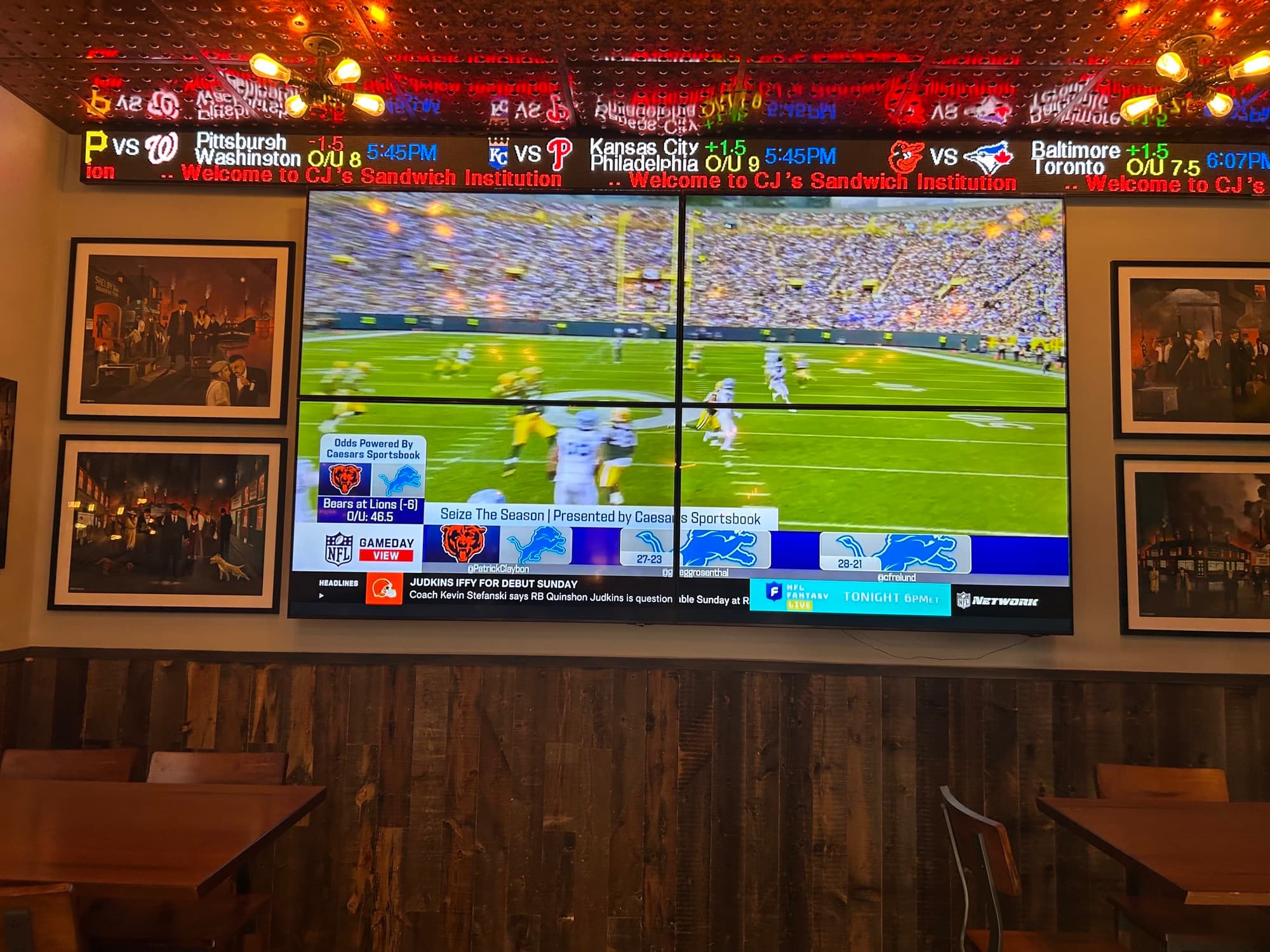 Large TV screen showing NFL games with CJ's Sandwich Institution welcome message at sports bar
