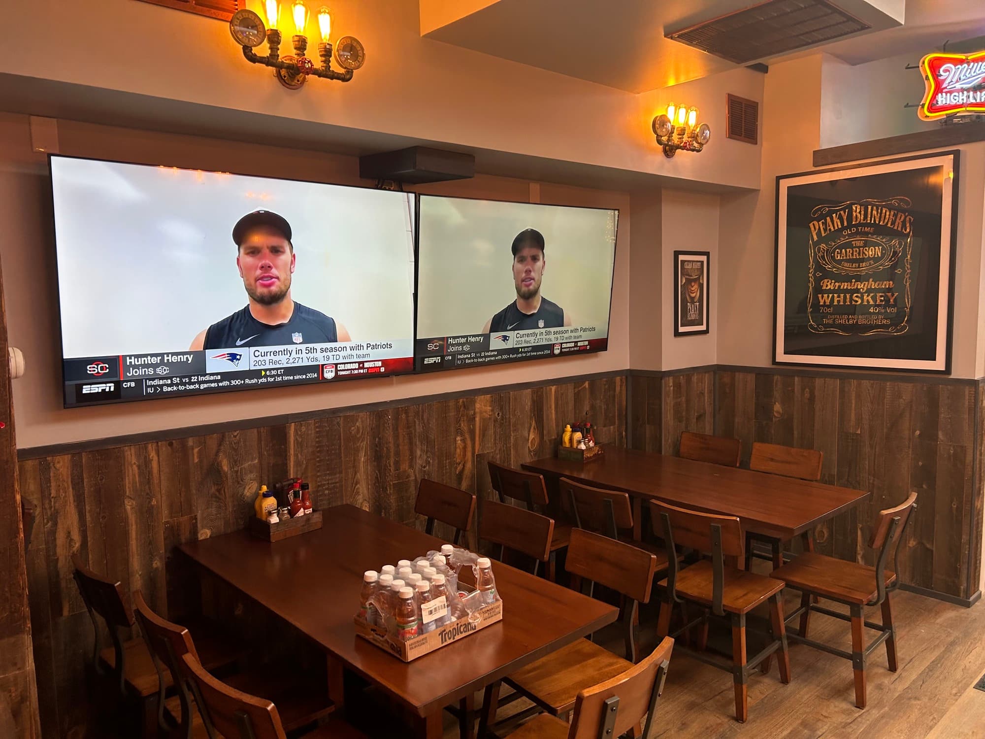 Sports bar seating area with dual TVs showing ESPN and Peaky Blinders whiskey decor
